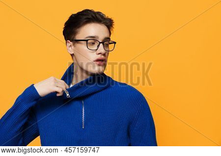 An Attractive Young Man Stands On An Orange Background In A Blue Zip-up Jacket And Black Eyeglasses 