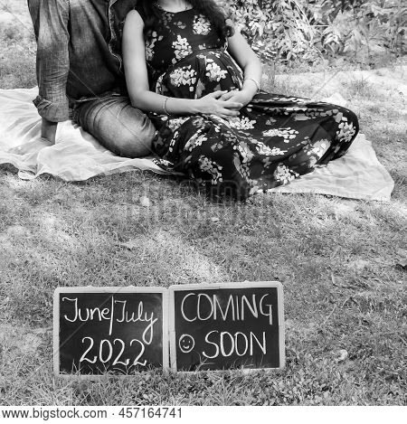 Indian Couple Posing For Maternity Baby Shoot. The Couple Is Posing In A Lawn With Green Grass And T