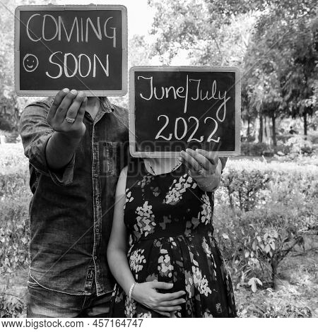 Indian Couple Posing For Maternity Baby Shoot. The Couple Is Posing In A Lawn With Green Grass And T