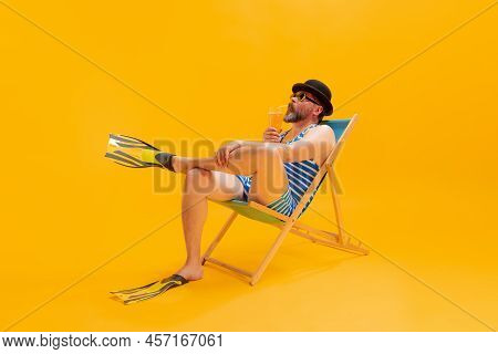 Studio Shoot Of Cool Funny Beachgoer, Man In Vintage Striped Swimsuit And Bowler Hat Sitting In Sunb