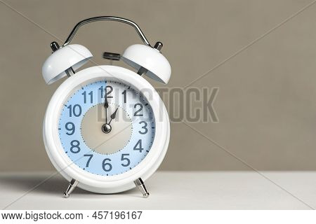 One Hour On The Alarm. A White Alarm Clock Is On A White Table. The Clock Hand Points To The Hour. T