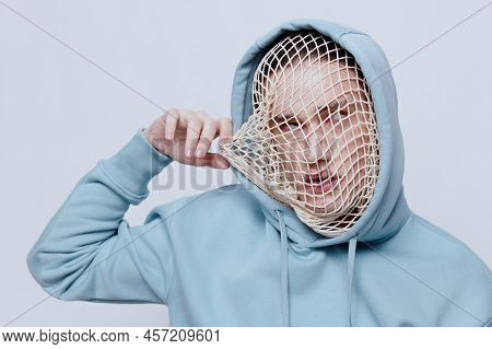 Tortured, Suffering From Problems, A Man With A Mesh On His Face Stands In A Light Blue Hoodie On A 