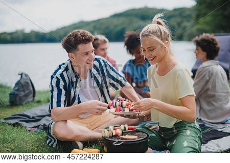 Group Of Multiracial Young Friends Camping In Campsite Near Lake And And Having Barbecue, Putting Sk