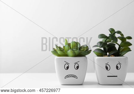 Beautiful Potted Houseplants With Angry And Concerned Faces On White Table, Space For Text. Emotiona