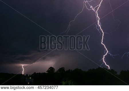 Night Photo Of Two Lightnings In The Sky Over A Small Village. One Lightning Close To The Viewer, Th