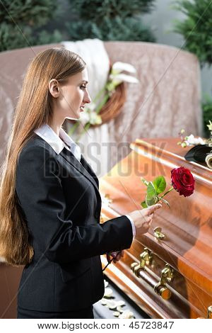 ผู้หญิงในงานศพกับยืนกุหลาบแดงที่หีบศพหรือหีบศพไว้อาลัย