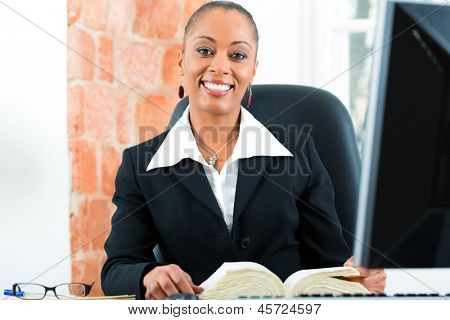 Junge weibliche Schwarze Anwältin arbeiten in ihrem Büro und lesen eine typische Gesetz-Buch vor einem compute