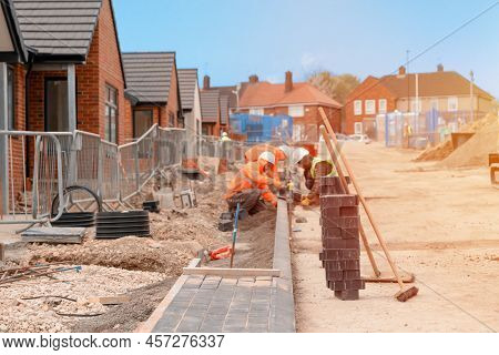 Builders Installing Paving Blocks During Road And Footpath Construction On A Semi-dray Concrete Mix.