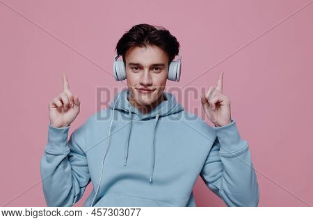 Horizontal Photo On A Pink Background Of A Funny Young Man In A Light Blue Hoodie, Pointing With His