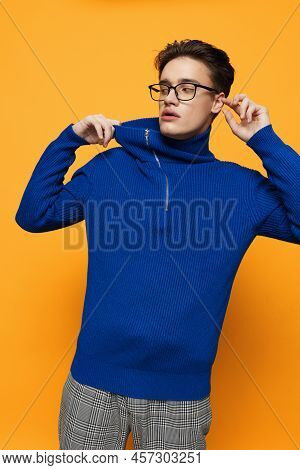 An Attractive Young Man Stands On An Orange Background In A Blue Zip-up Jacket And Black Eyeglasses 