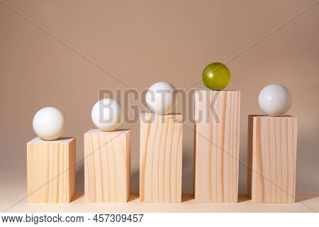 Prominent Yellow Sphere Among White Spheres On Wooden Bars On Pastel Beige Background. The Differenc