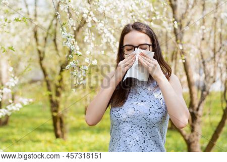 Portrait Of An Allergic Young Girl In The Park Holding White Napkin And Sneezing Because Of Allergy 
