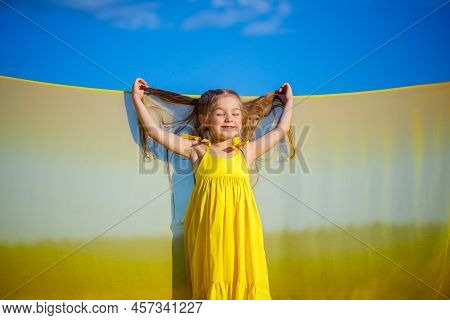 Ukrainian Girl 7 Years Old, She Is A Patriot Of Ukraine, Dressed In A Yellow Dress Against A Blue Sk