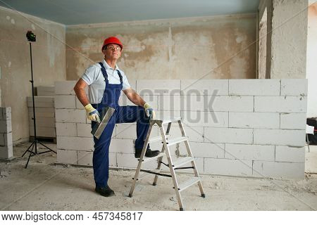 Professional Construction Worker In Uniform Standing With Spatula On Step Ladder. Portrait Of Contra
