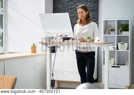 Woman Using Adjustable Height Standing Desk In Office For Good Posture