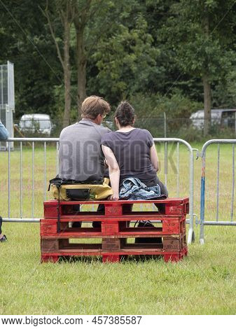 Hulst, Netherlands, June 26, 2022, Couple Sitting Side By Side On Red Stacked Wooden Pallets