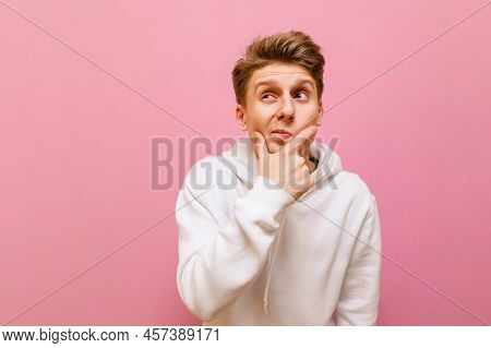 Funny Pensive Guy In White Casual Clothes Stands On A Pink Background, Looks Away At A Blank Spot Wi