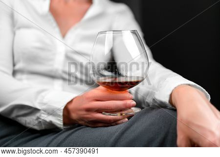 Drinking Glass Filled With Alcohol Held By Woman In Business Clothes Sitting With Her Legs Crossed. 