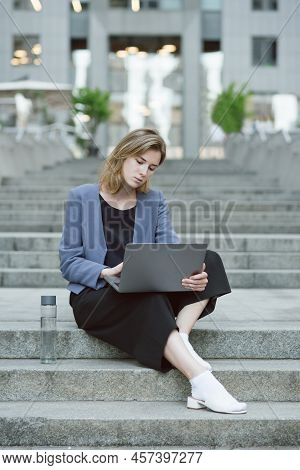 Vertical Potrait Of A Concentrated Young Businesswoman Working At Her Laptop. Bottle Of Water Near T