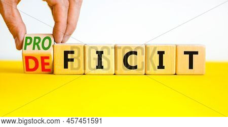 Proficit Or Deficit Symbol. Businessman Turns Wooden Cubes And Changes The Concept Word Deficit To P