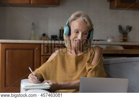 Older Woman In Headphones E-learning Online At Home Use Laptop