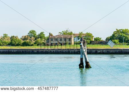 Abandoned And Broken House In The Venice Lagoon, And Three Big Wooden Poles Implanted In The Seabed 