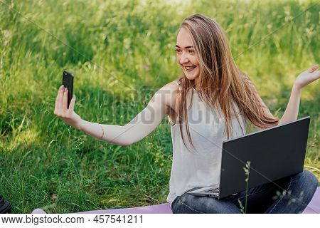 Girl Sits Outdoors And Works At A Laptop. Makes A Video Call On The Phone. Freelance. Selfeducation.