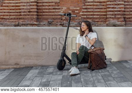 Woman In White Sneakers And Leather Backpack Sitting On Electric Scooter