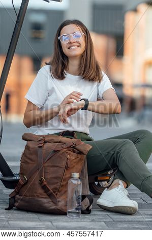 Woman In White Sneakers And Leather Backpack Sitting On Electric Scooter