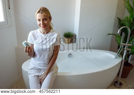 Beautiful Young Blonde Happy Woman Sitting In Bathroom And Holding Brush Cleanser.
