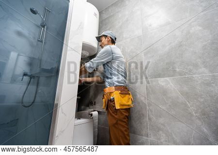 Plumber Installing Electric Heating Boiler. Young Handyman In Uniform Setting Up Electric Heating Bo
