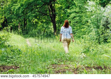 Portrait Of Young Buxom Woman With Long Curly Red Hair Walking In Park Forest Among Green Trees Bush