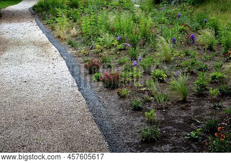 Beds Of Newly Planted Flowers Are Planted And Mulched With Bark. Bluebells And Cypresses, Paths Stre
