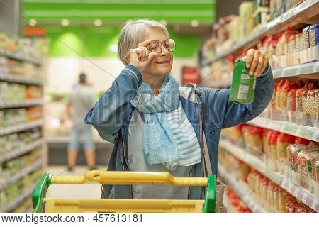 Portrait Smiling Senior Woman Making Purchases In The Supermarket Selecting Checking A Product. Cauc