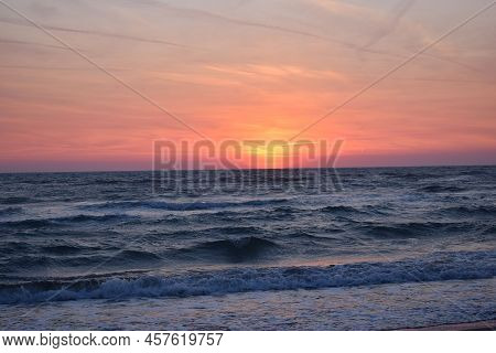 A Beautiful Sunset On The Beach In The Turbulent Ocean. Shades Of Orange And Blue.
