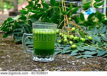 Neem Medicinal Herb Juice In Glass Cup. Neem Leaves, Fruits On Abstract Background. Ayurvedic Raw Ma