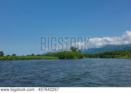 The Bed Of The Blue River Bends Between The Green Banks. A Picturesque Mountain Range Against The Ba