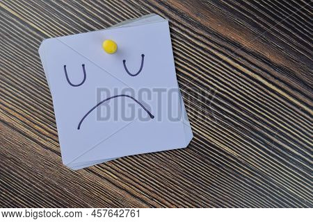 Concept Of Unhappy Booring Moody Emotion Face Write On Sticky Notes Isolated On Wooden Table.