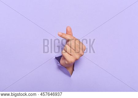 Human's Hands Showing Symbol Korean Mini Heart Gesure Through The Torn Holes Of Purple Paper Backgro