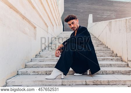 Full Body Of Feminine Man With Rhinestones On Face In White High Heeled Boots Looking At Camera Whil