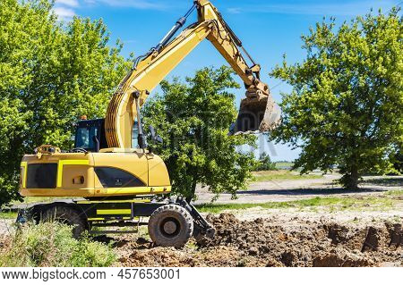 An Excavator Digs A Pond Pit In The Garden Against The Blue Sky. Digging A Pit With An Excavator. Ea