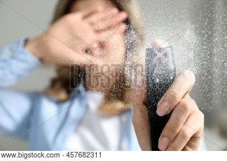 Young Woman Covering Eyes With Hand And Using Pepper Spray At Home