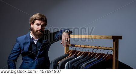 Stylish Mens Suit. Workshop. Handsome Bearded Fashion Man In Classical Costume Suit. Male Suits Hang