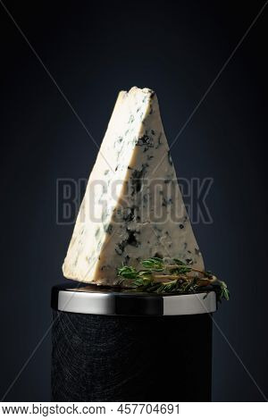 Triangle Piece Of Blue Cheese With Thyme On A Black Background.