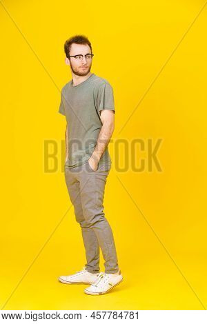 Young Man Wears Eye Glasses In Casual Wear Posing On Yellow Background With Hands In Pockets Looking