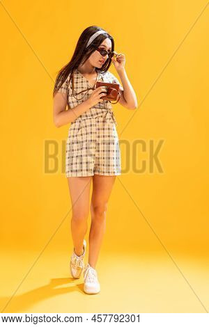 Portrait Of Beautiful Stylish Girl Taking Photo With Vintage Camera Isolated Over Yellow Studio Back