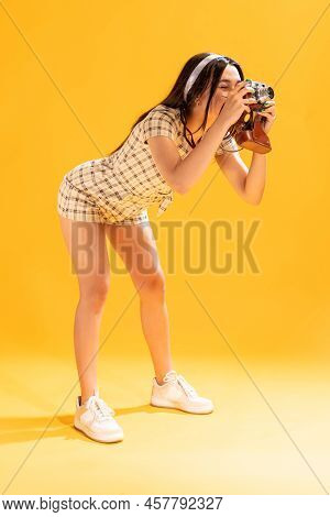 Portrait Of Beautiful Stylish Girl Taking Photo With Vintage Camera Isolated Over Yellow Studio Back