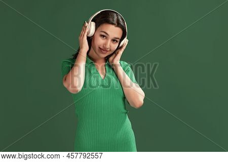 Portrait Of Beautiful Young Girl Listening To Music In Headphones, Posing Isolated Over Green Studio