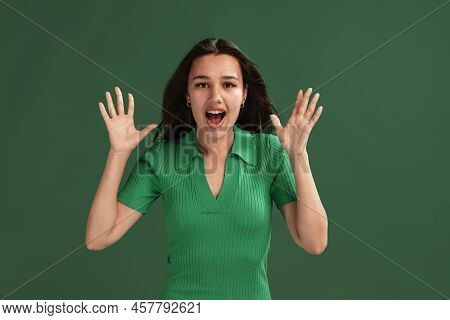 Portrait Of Emotive Young Girl Posing, Showing Shocked Face Isolated Over Green Studio Background
