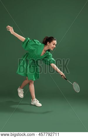 Portrait Of Cheerful Young Girl Posing In Dress, Playing Badminton Isolated Over Green Studio Backgr